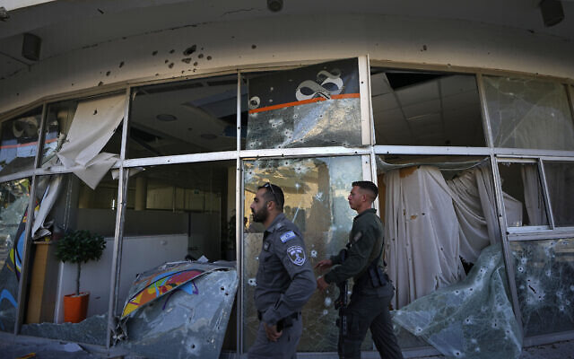 Israeli security forces walk next to a bank damaged by rocket fire from Lebanon in Shlomi, northern Israel, near the Lebanese border, Thursday, April 6, 2023. The branch was closed for Passover. (AP Photo/Ariel Schalit)