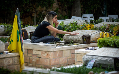 A woman sits next to a grave of fallen soldier in the Mount Herzl Military Cemetery in Jerusalem, on April 19, 2023, ahead of Memorial Day next week. (Yonatan Sindel/Flash90)