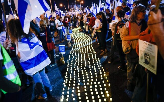 Bereaved families and Israelis stand next to memorial candles during a protest against the Israeli government's planned judicial overhaul in Tel Aviv on April 22, 2023. (Erik Marmor/Flash90)