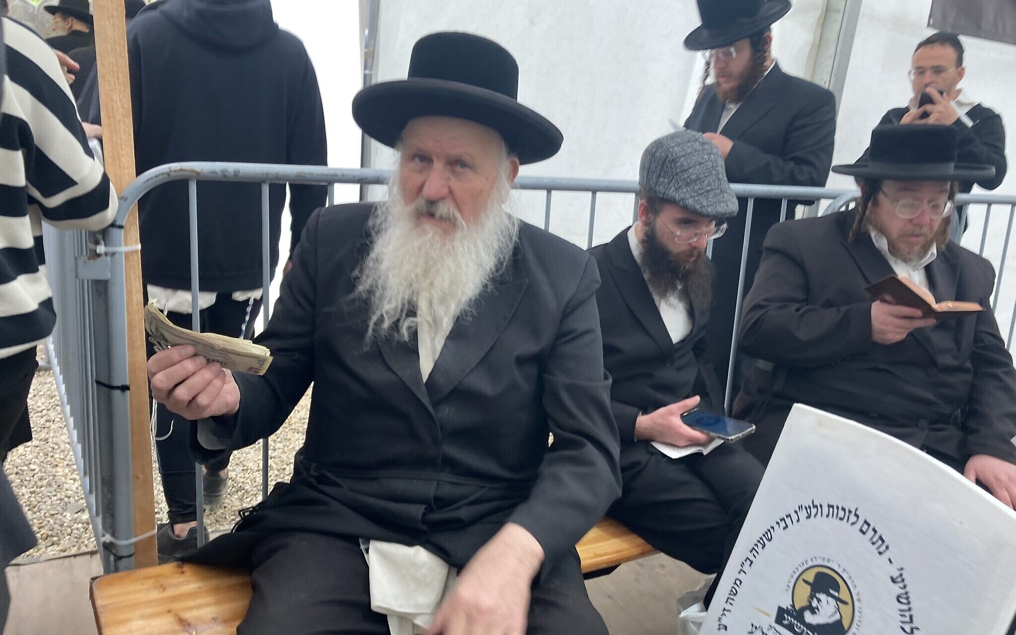 A man collect charity near the gravesite of 'Wonder Rabbi' Yeshaya Steiner in Bodrogkeresztur, Hungary, April 24, 2023. (Yaakov Schwartz/ Times of Israel)