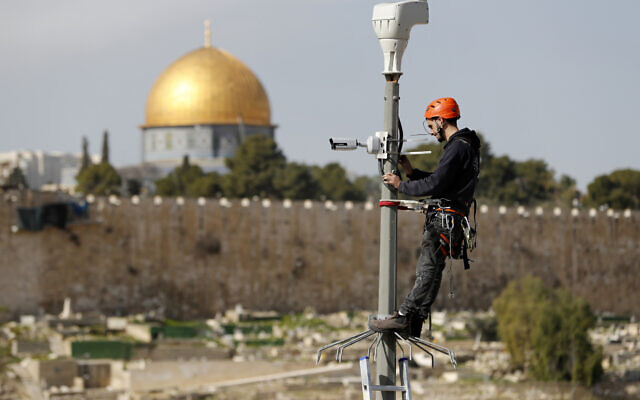 An Israeli technician climbs up a pole to install a surveillance camera on a street in the east Jerusalem neighborhood of Ras al-Amud on January 24, 2019. (AHMAD GHARABLI / AFP)