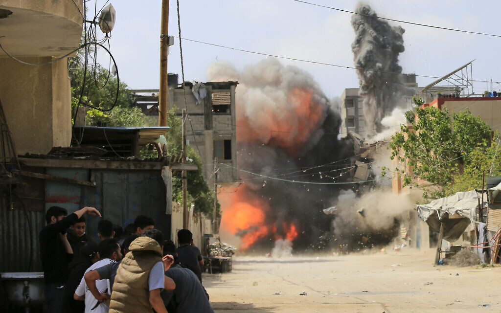 People take cover behind a wall as a building in Beit Lahia in the northern Gaza Strip is hit by an Israeli airstrike, targeting an Islamic Jihad commander, on May 12, 2023. (Bashar Taleb/AFP)