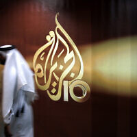 Illustrative: An employee of Al Jazeera walks past the channel's logo at its headquarters in Doha, Qatar, in 2006. (AP/ Kamran Jebreili, File)