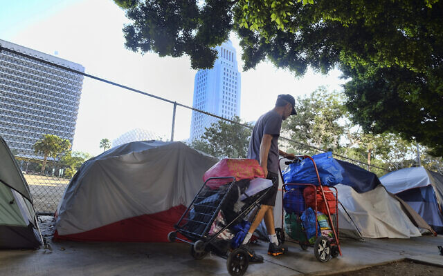 A homeless man moves his belongings from a street behind Los Angeles City Hall as crews prepared to clean the area on July 1, 2019. (AP Photo/Richard Vogel, File)