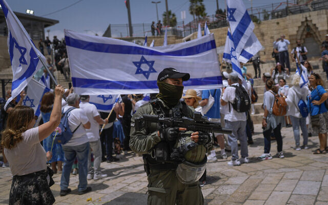 A police officer stands guard as Israelis wave flags ahead of a march marking Jerusalem Day, in front of the Damascus Gate of Jerusalem's Old City, May 18, 2023. (AP Photo/Ohad Zwigenberg)