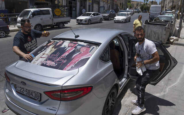 A printing specialist laminates a Jordanian vehicle with pictures of, from right, King Abdullah II, Crown Prince Hussein, Saudi architect Rajwa Alseif and Queen Rania, in the capital Amman, Jordan, May 31, 2023. (Nasser Nasser/AP)