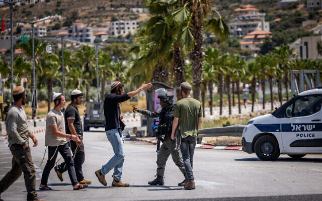 Israeli security forces argue with Israeli settlers at the entrance to the West Bank village of Turmus Ayya on the day that Jewish extremists set fire to homes and vehicles in the town, June 21, 2023. (Yonatan Sindel/Flash90)