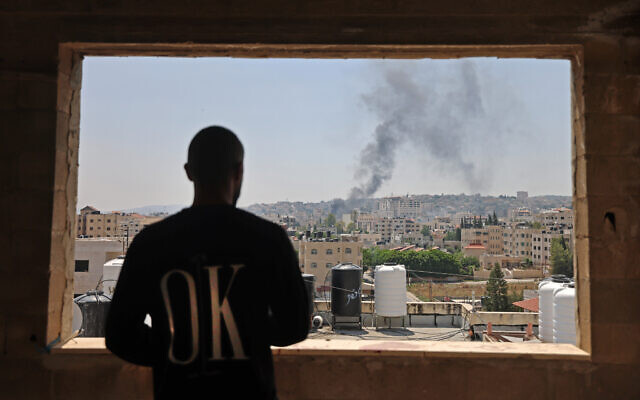 A Palestinian man looks out the window as smoke billows following an Israeli drone strike in the West Bank city of Jenin, on July 3, 2023. (Photo by Jaafar ASHTIYEH / AFP)