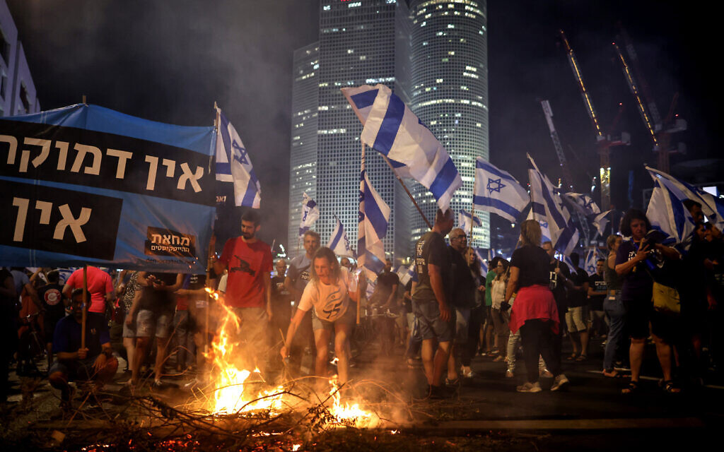 Anti-government protesters raise flags and light a fire on the Ayalon Highway in Tel Aviv, following the resignation of Tel Aviv police chief Ami Eshed, on July 5, 2023. (Oren Ziv/AFP)