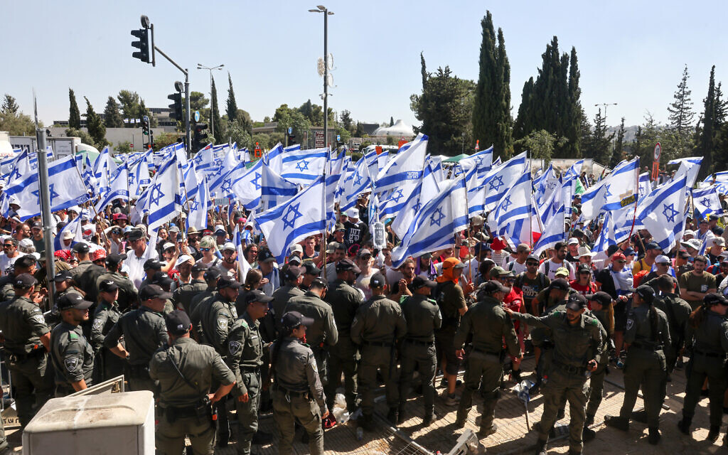 Police forces stand guard as protesters wave flags at the entrance of the Knesset in Jerusalem on July 24, 2023. (Menahem KAHANA / AFP)