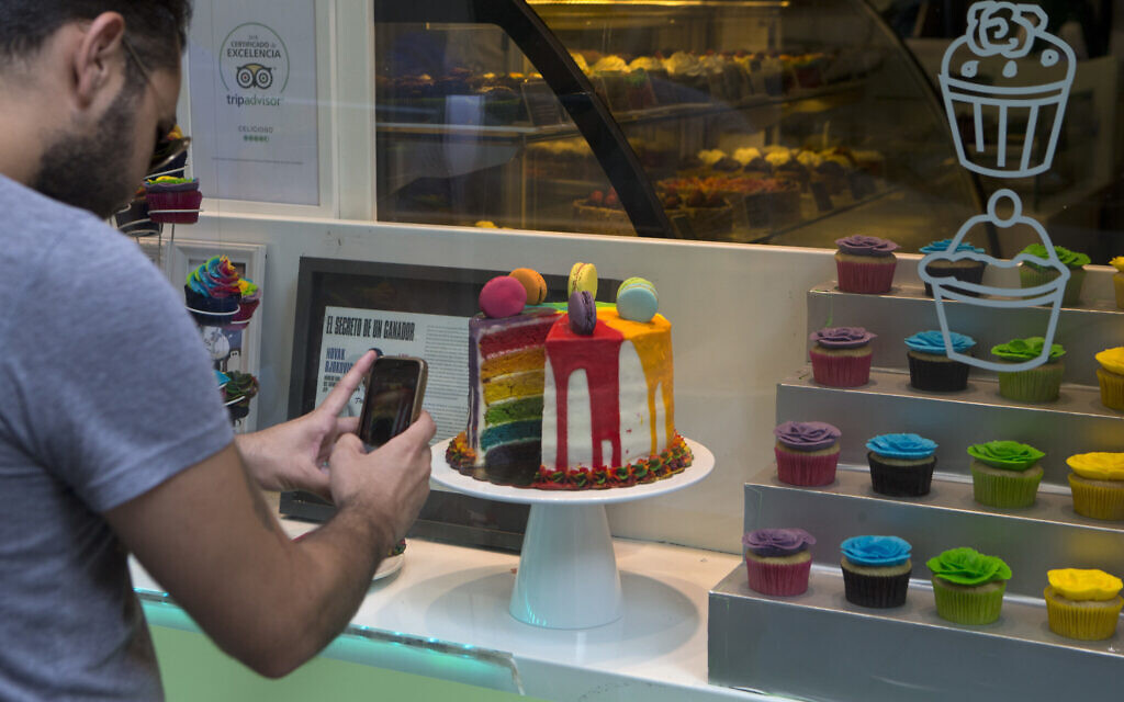 Illustrative: a man takes a photo of a multicoloured cake in a window display of a cake shop. (AP Photo/Paul White)