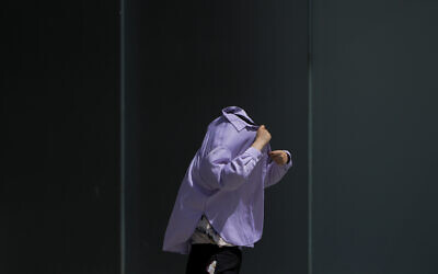 A woman uses a long-sleeve shirt to shield from the sun as she walks at an outdoor shopping mall on a sweltering day in Beijing, July 6, 2023. (Andy Wong/AP)