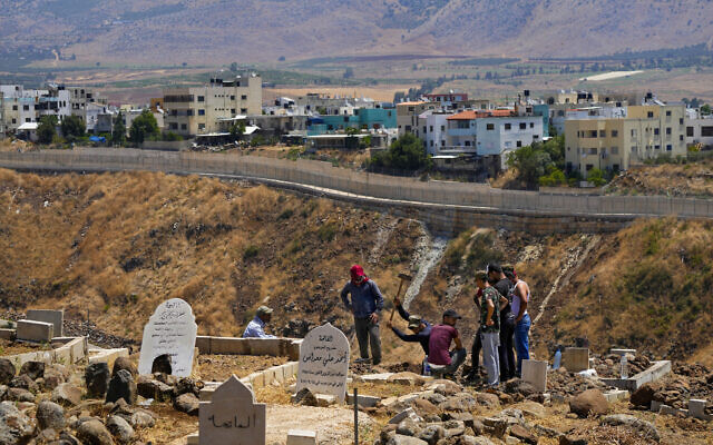 Residents dig a grave at a cemetery on the Lebanese side of the Lebanese-Israeli border in the southern village of Wazzani with the walled northern part of Ghajar village in the background, Lebanon, Tuesday, July 11, 2023. (AP Photo/Hassan Ammar) Residents dig a grave at a cemetery on the Lebanese side of the Lebanese-Israeli border in the southern village of Wazzani with the walled northern part of Ghajar village in the background, Lebanon, Tuesday, July 11, 2023. (AP Photo/Hassan Ammar)