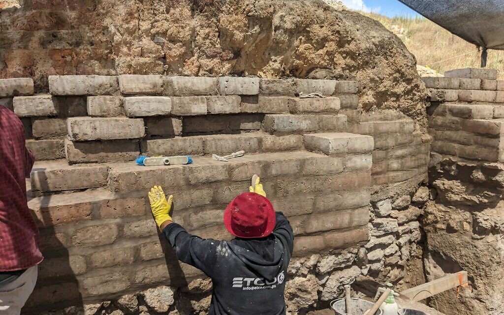 An IAA conservationist puts the finishing touches on a wall that strengthens the opening to the Canaanite Gate at Tel Gezer, at what was once a major entrance to the fortified city, on July 6, 2023. (Melanie Lidman/Times of Israel)