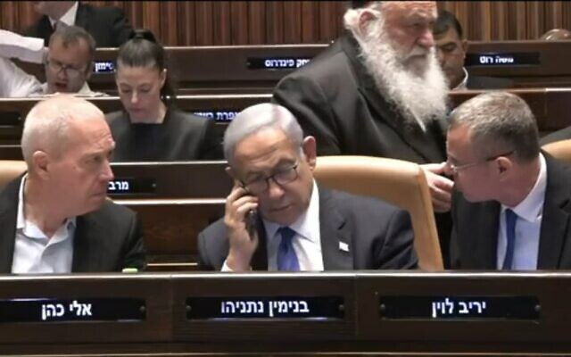 Prime Minister Benjamin Netanyahu (center) speaks on his phone in the Knesset as Justice Minister Yariv Levin (right) and Defense Minister Yoav Gallant talk across him, during the vote on the "reasonableness" law in the Knesset, July 24, 2023. (Channel 12 screenshot)