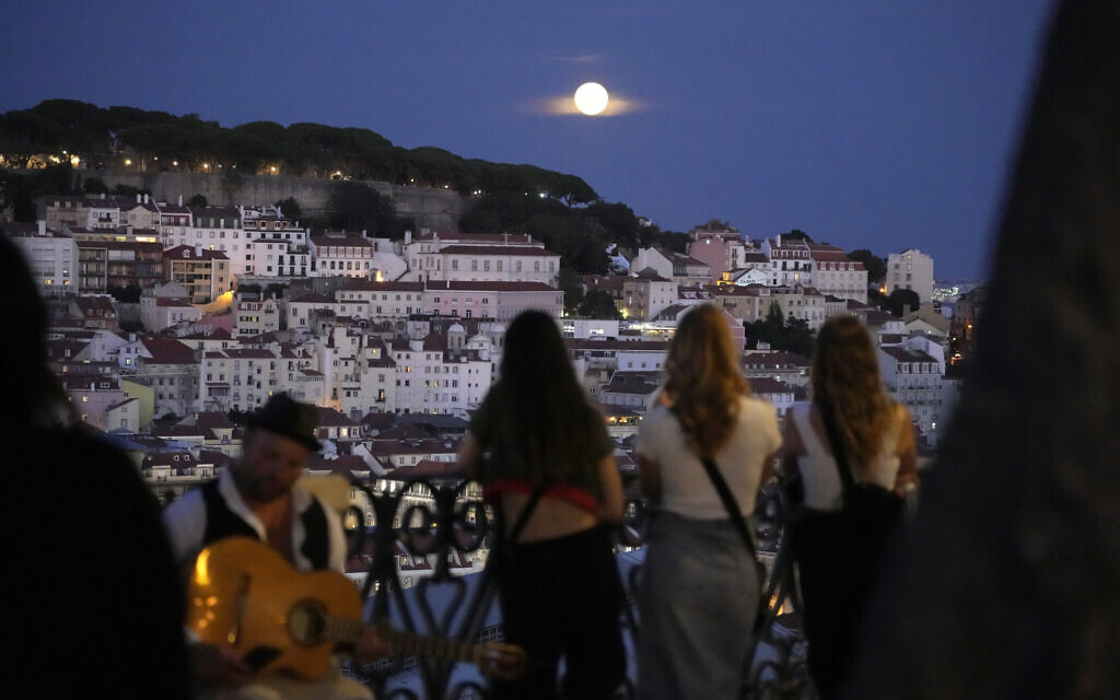 People watch a supermoon rise above Lisbon, August 30, 2023. (Armando Franca/AP)