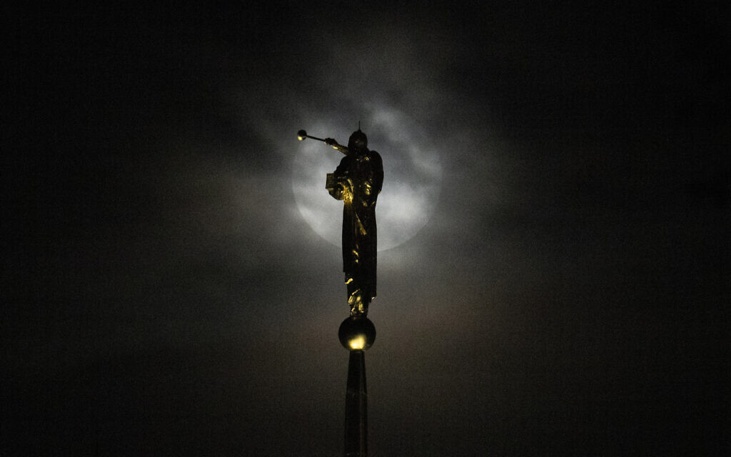 The blue supermoon rises behind a thick layer of clouds near a statue of the angel Moroni perched atop The Church of Jesus Christ of Latter-day Saints, in Kensington, Maryland, August 30, 2023. (Julio Cortez/AP)
