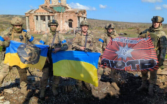 This handout photograph released by Ukrainian presidential chief of staff Andriy Yermak on September 17, 2023, shows Ukrainian servicemen posing for a photo with Ukrainian national flags in front of a destroyed building in the village of Klyshchiivka, Donetsk region.(Photo by Handout / Ukrainian Presidential Chief of Staff Andriy Yermak / AFP)