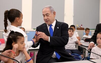 Prime Minister Benjamin Netanyahu looks at a plastic bracelet as he visits first graders in Ma'ale Adumim, September 1, 2023. (Avi Ohayon/GPO)