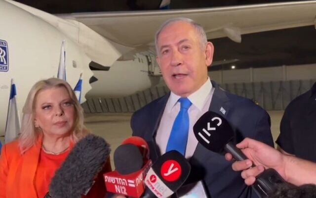 Prime Minister Benjamin Netanyahu, with his wife Sara at his side, speaks to reporters as they prepare to board a plane for the US early Monday, September 18, 2023. (Channel 12 screenshot)
