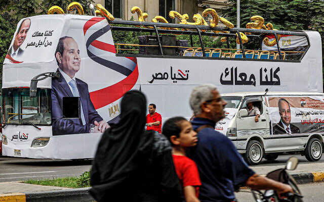 A man, child, and woman ride a motorcycle across the street from an election campaign bus for Egypt's President Abdel Fattah al-Sisi adorned with his image, his slogan 'long live Egypt,' and C-shaped balloons, as Sisi's supporters prepare for a rally outside the Cairo University campus in Giza, the twin-city of the Egyptian capital, on October 2, 2023. (Khaled Desouki/AFP)