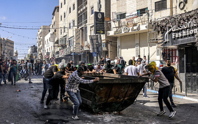 Palestinian protesters push a dumpster to be used for cover during clashes with Israeli forces following a rally in solidarity with Gaza by supporters of the Fatah and Hamas movements, in the city of Hebron in the West Bank on October 13, 2023.(HAZEM BADER / AFP)