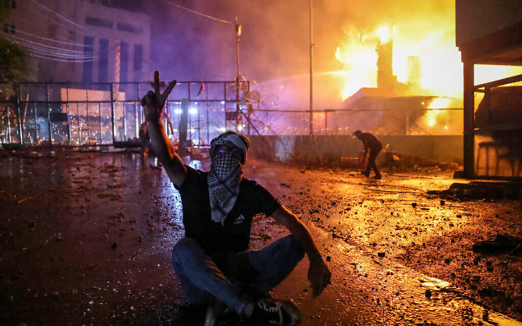 A Lebanese protester flashes the V for victory sign on October 18 as a fire rages behind the security gate of the US embassy after clashes with security forces during a demonstration in solidarity with the people of Gaza in Awkar, east of Beirut on October 17, 2023. (JOSEPH EID / AFP)