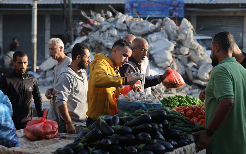 People buy vegetable from a stall set up in front of the rubble of a destroyed building at a market in Rafah in the southern Gaza Strip on October 20, 2023, amid ongoing battles between Israel and Hamas terrorists. (Photo by MOHAMMED ABED / AFP)