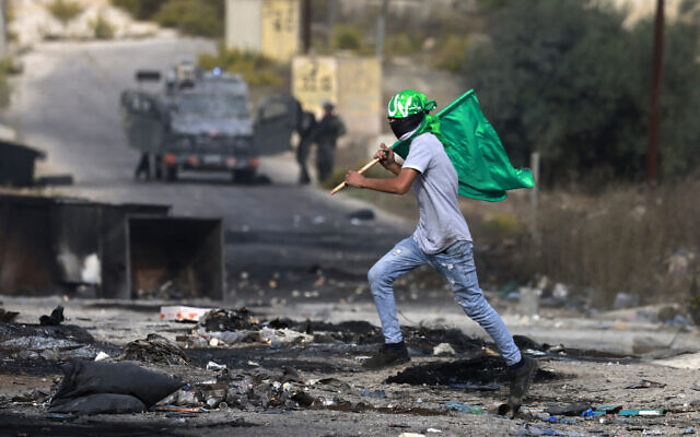 A Palestinian waves a Hamas flag during clashes with Israeli troops at the northern entrance of the West Bank city of Ramallah, near the Israeli settlement of Beit El on October 27, 2023. (Jaafar Ashtiyeh/AFP)