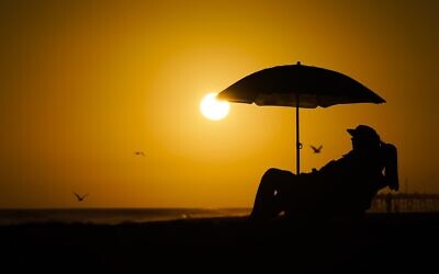 FILE - A person rests under an umbrella as the sun sets, September 12, 2023, in Newport Beach, California. (AP Photo/Ryan Sun, File)