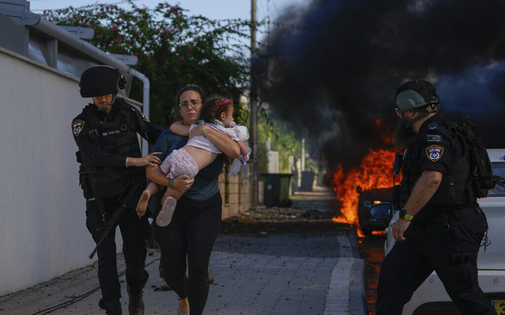 Police officers evacuate a woman and a child from a site hit by a rocket fired from the Gaza Strip, in Ashkelon, October 7, 2023. (AP Photo/Tsafrir Abayov)
