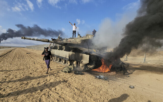 Palestinians celebrate by a destroyed Israeli tank at the Gaza Strip fence east of Khan Younis, October 7, 2023. (AP Photo/Hassan Eslaiah)