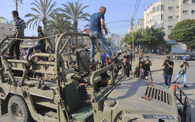 Palestinians ride on an Israeli military vehicle taken from an army base overrun by Hamas terrorists near the Gaza Strip fence, in Gaza City, October 7, 2023. (Abed Abu Reash/AP)