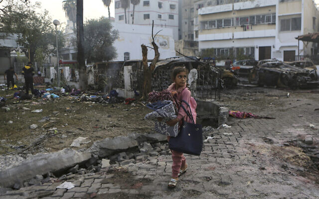 A girl carries blankets as she walks past the site of a deadly explosion near al-Ahli hospital in Gaza City, Wednesday, Oct. 18, 2023. (AP Photo/Abed Khaled)