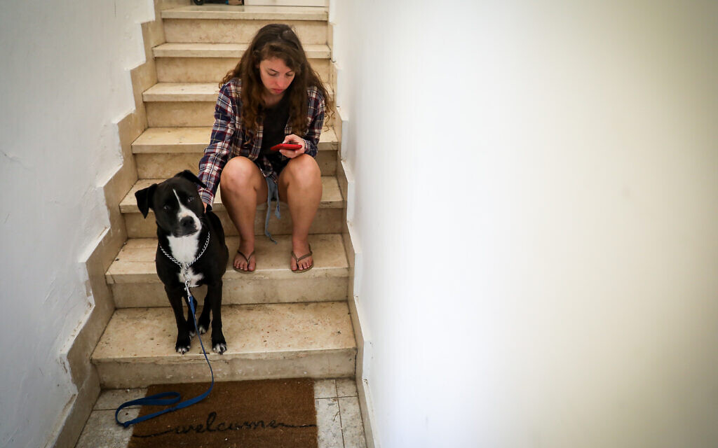 Illustrative: A woman and her dog take cover in a stairway in Jerusalem, as a red alert siren sounds during a rocket barrage fired from Gaza into Israel, October 7, 2023. (Noam Revkin Fenton/Flash90)