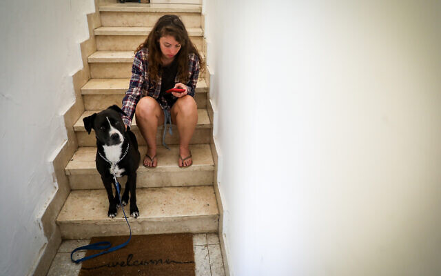 A woman and her dog take cover in a stairway in Jerusalem, as a red alert siren sounds during a rocket barrage fired from Gaza into Israel, October 7, 2023. (Noam Revkin Fenton/Flash90)