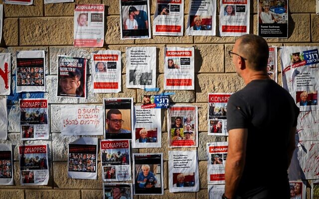 People walk near posters featuring Israelis being held hostage by Hamas in Gaza, outside the Defense Ministry in Tel Aviv, October 18, 2023. (Chaim Goldberg/Flash90)
