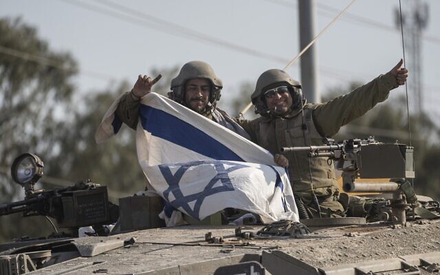 Soldiers wave as they hold an Israeli flag on top of a tank near the border with Lebanon, October 14, 2023. (AP Photo/Petros Giannakouris)