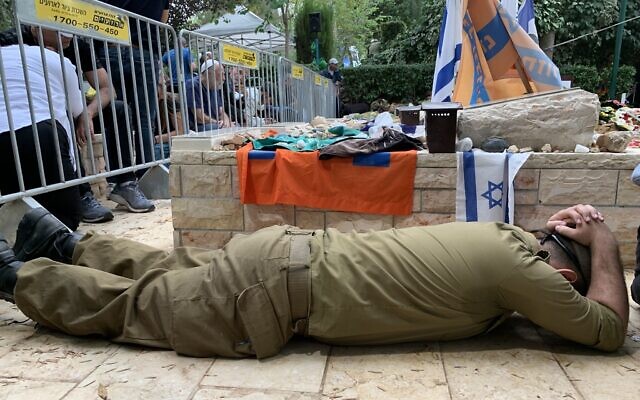 Soldier takes cover with hands above head after hearing rocket sirens during funeral of lone soldier Cpl. Netanel Young. (Charlie Summers/Times of Israel)