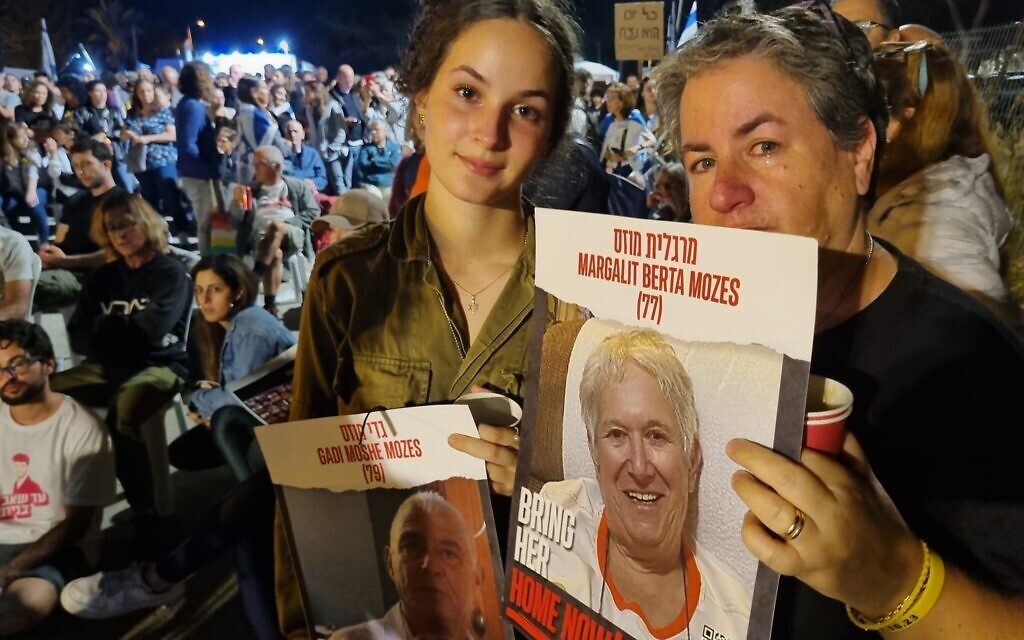 Shani Mozes (left) holds up a photo of her grandfather who was kidnapped from Kibbutz Nir Oz, Shani’s mother holds up a photo of her grandmother, November 14, 2023. (Bernard Dichek/Times of Israel)