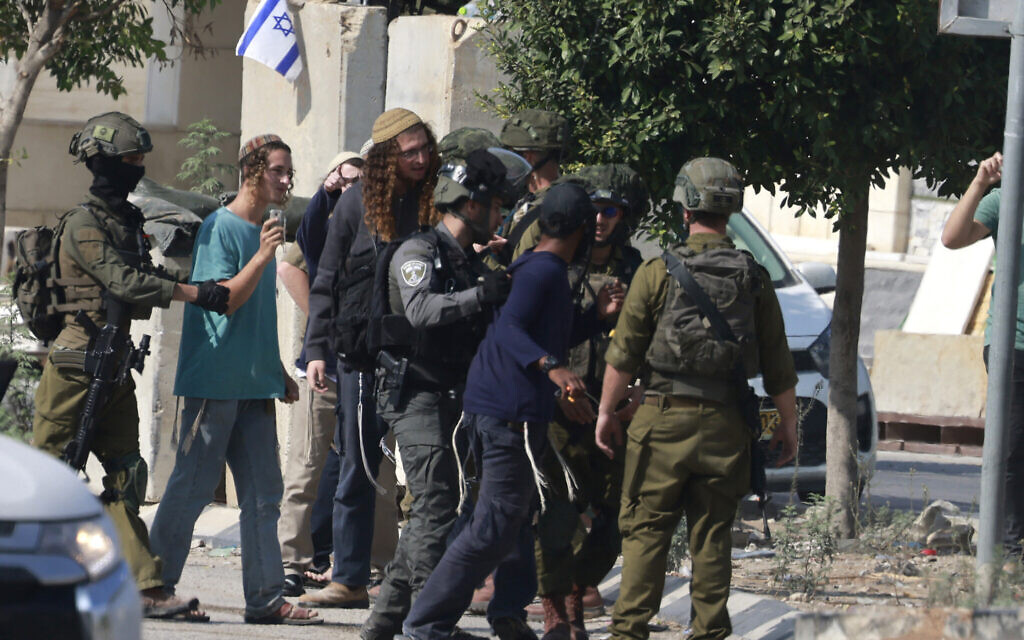Israeli soldiers restrain Jewish settlers after they stormed the Palestinian West Bank village of Dayr Sharaf following a terror attack in which an Israeli driver was shot dead, November 2, 2023. (Jaafar Ashtiyeh/AFP)