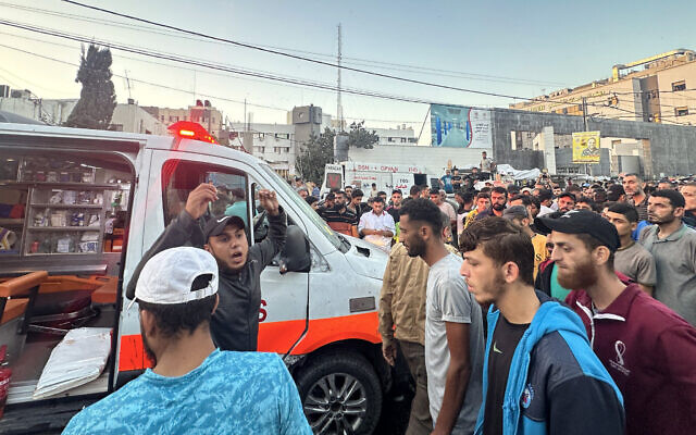People gather around an ambulance damaged in an Israeli airstrike in front of Al-Shifa hospital in Gaza City on November 3, 2023. The IDF said it struck an ambulance that was being used by a Hamas cell, and killed several Hamas operatives. (MOMEN AL-HALABI / AFP)