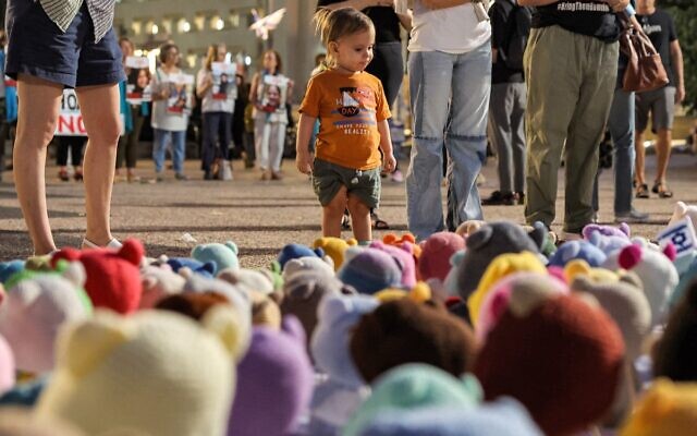 A child looks on as people stand before small teddy bears placed at a sit-in demanding government action for the hostages, outside the Kirya military headquarters in Tel Aviv, November 7, 2023. (JACK GUEZ / AFP)