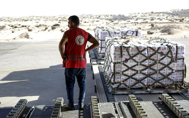 An Egyptian Red Crescent member stands next to a shipment of humanitarian aid bound for the Gaza Strip unloaded off a Qatar Emiri Air Force C-17 Globemaster III military transport aircraft after landing at Arish International Airport in North Sinai province in northeastern Egypt on November 9, 2023 (Karim JAAFAR / AFP)