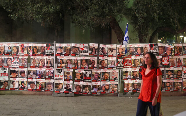 Illustrative: A woman walks past portraits of Israelis taken hostage by Palestinian terrorists in the October 7 attack, during a demonstration calling for their release in Tel Aviv on November 13, 2023. (Ahmad Gharabli/AFP)