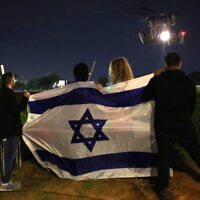 People wave an Israeli flag as a helicopter transporting newly released hostages, held since the Gaza-ruling Hamas terror group's October 7 attack, lands outside Sheba Medical Center in Ramat Gan on November 28, 2023. (Jack Guez/AFP)