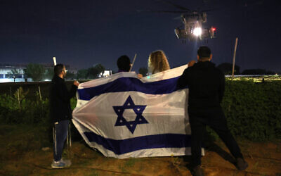 People wave an Israeli flag as a helicopter transporting newly released hostages, held since the Gaza-ruling Hamas terror group's October 7 attack, lands outside Sheba Medical Center in Ramat Gan on November 28, 2023. (Jack Guez/AFP)