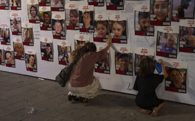 An woman touches photos of Israelis missing and held captive in Gaza, displayed on a wall in Tel Aviv, on Oct. 21, 2023 (AP Photo/Petros Giannakouris)