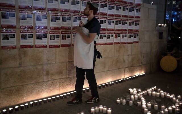 A man 'wears' his baby as he looks at posters of the men, women and children held hostage by Hamas in the Gaza Strip, during a vigil marking 30 days since the October 7 Hamas onslaught that started the fighting, in Jerusalem, on November 5, 2023. (AP Photo/Maya Alleruzzo)