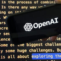 The OpenAI logo appears on a mobile phone in front of a screen showing a portion of the company website in New York, November 21, 2023. (Peter Morgan/AP)
